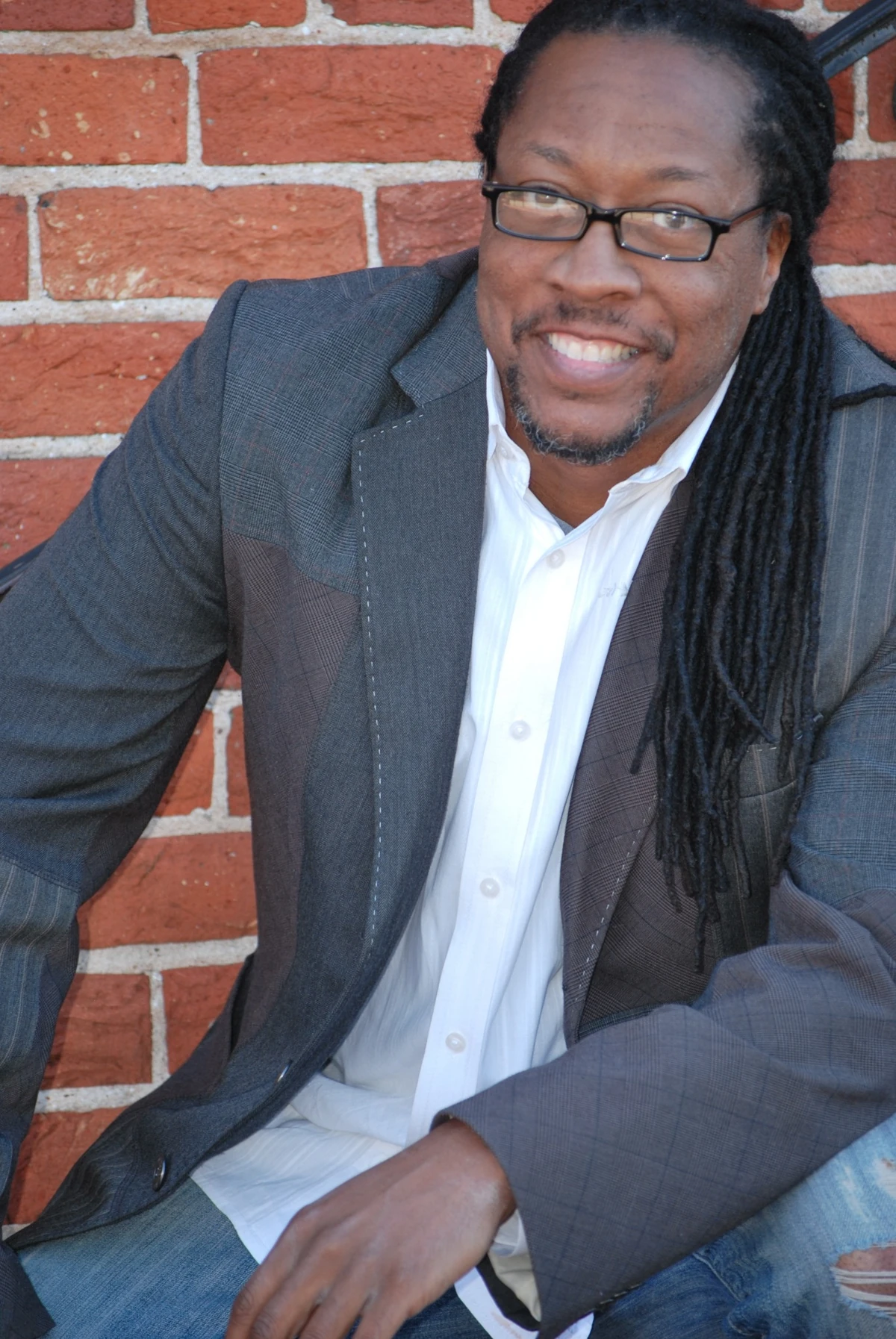 Antonio Thornton smiling in a gray jacket and white shirt beside a brick wall